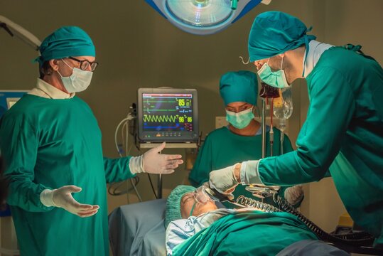 Team of surgery doctor using defibrillator pump chest heart patient to save life while medical surgery in operating room at emergency CPR. Defibrillator in surgeon specialist hand. - Powered by Adobe