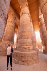 A blonde woman wearing a stylish hat examines the large columns at Karnak temple - Karnak temple in...