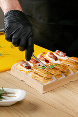 A person in black gloves arranging gourmet canapes with prosciutto and sun-dried tomatoes,...