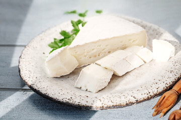 Delicious brie and camembert cheeses on a handmade clay kraft plate. Dairy French products. background blue board