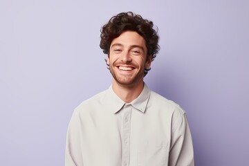 A man in a pale yellow sweater beaming on a gentle lavender background.