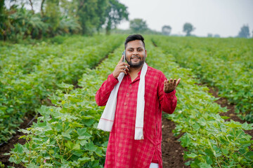 An Indian farmer is speaking on a phone in a field of agriculture.