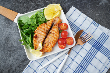 Grilled Butterfly Salmon Steak with cherry tomatoes and arugula salad on a white square plate....