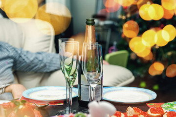 Christmas table setting with Christmas tree in the background. The table is ready for a festive dinner and party with champagne and sandwiches with caviar