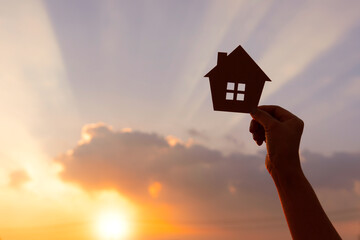 woman hands holding paper house on sunrise, family home, homeless housing, home protection...