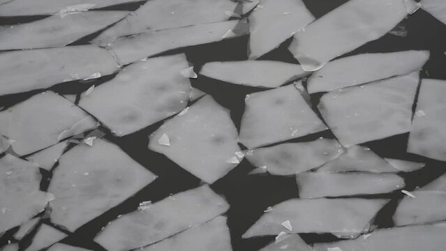 Abstract winter natural background. Top view of grey ice drift on river in a cloudy day. Ice floes of different sizes floats on water surface. Real time handheld video. Springtime theme.