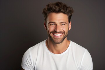 Handsome tanned smiling young man in a white T-shirt on brown background - obrazy, fototapety, plakaty