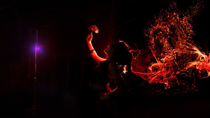 the silhouette of a female dancer holding sparkling jewelry and looking sharp in the dark with fire burning in the background - obrazy, fototapety, plakaty
