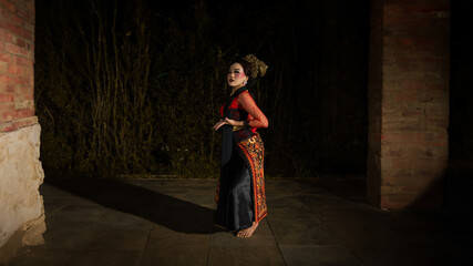 an Indonesian dancer wearing jewelry that shines under the spotlight of the stage lights adds to...