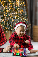 Fototapeta na wymiar Family. A beautiful little blond boy of 1 year old is sitting on the background of a Christmas tree. The concept of celebrating Christmas and New Year 2024.