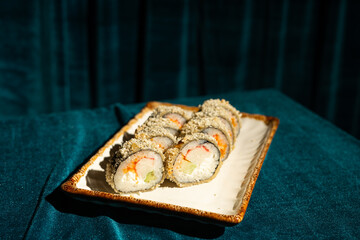 Oriental restaurant menu. Hot sushi on blue velvet background. Maki roll with shrimp and avocado on white plate. Modern, stylish Japanese cuisine.