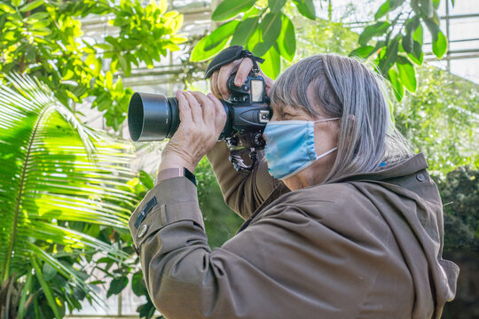 old woman with mask taking photos in botanical garden