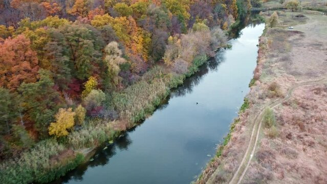 Aerial forward flight above river with vibrant colorful trees on riverbanks. Autumn on Siverskyi Donets river with calm water in Ukraine