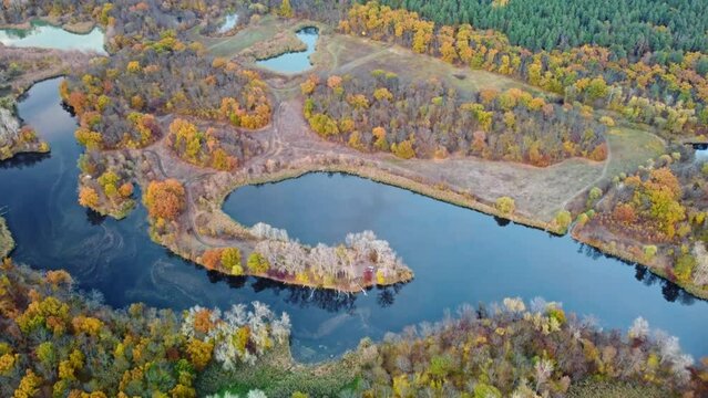 Autumn aerial look down view on river valley with vivid trees on riverbanks. Autumnal nature with calm blue mirror water surface