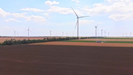 Wind turbines rotate gracefully, generating clean electricity for the nearby communities. A wheat combine harvester diligently works in the field. A harmony between technology and nature. - Powered by Adobe