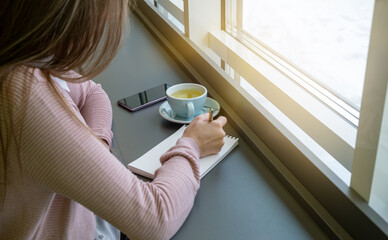 Young woman hands writing to do list in diary planning using journal reminder in cafe closeup. Have...