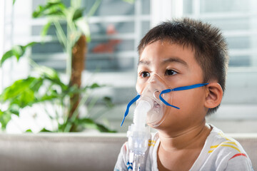 Asian Child using nebulizer mask equipment alone have smoke, Kid boy making makes inhalation nebulizer steam sick cough at home, oxygen spray inhaler therapy, stuffy nose and runny, Health medical - obrazy, fototapety, plakaty
