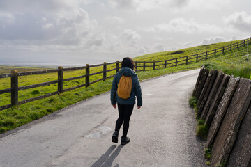 Woman with backpack walks slowly away along a path with go to the side in a typically Irish...