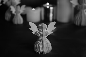 DIY paper angel on a dark background. Religious symbols, festive Christmas and New Year decor. Black and white artistic low key photo. Burning candles