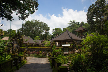A tranquil scene at a Balinese temple courtyard with traditional architecture, shrubbery, and ceremonial umbrellas.