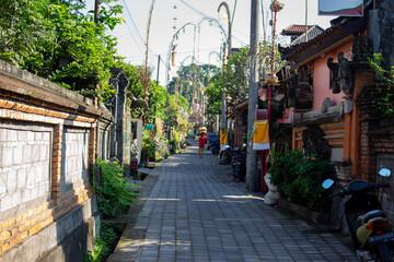 A quiet street in a tropical location flanked by walls and traditional buildings with scooters parked along the side.