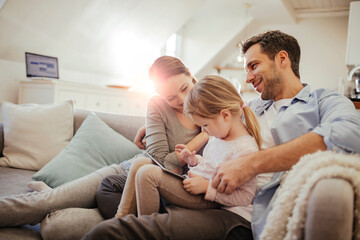 Happy young family sitting on couch with tablet