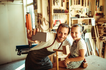 Father and daughter taking a selfie in a woodworking workshop - obrazy, fototapety, plakaty