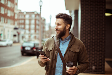Man enjoying his coffee while using a smartphone on a city street
