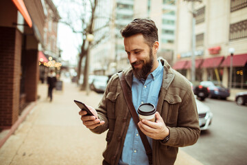 Man enjoying his coffee while using a smartphone on a city street
