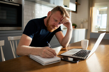 Contemplative man working from home with his laptop and notebook