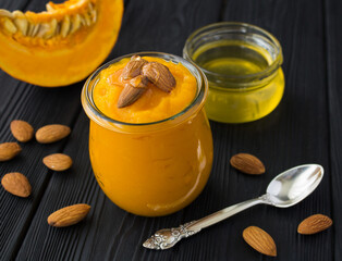 Puree with pumpkin, almond nut and honey in the glass jar on the black wooden background. Close-up.