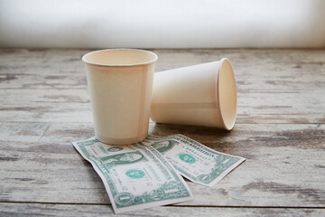 Empty paper cups under which two dollars lie, tips for service, coffee donations