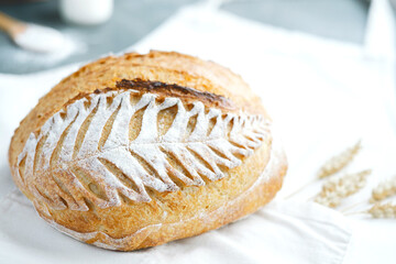 Homemade baked sourdough bread on scoring leaf pattern on the apron with ears of wheat. Cooking of healthy bread from alternative flours.