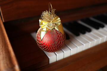 a red Christmas tree ball with a golden bow lies on the background of a piano. Christmas Card