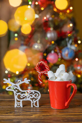 Christmas background with a Christmas tree, hot chocolate and marshmallows in a red mug. Selective focus.