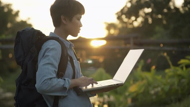 portrait of a beautiful asiatic solo travel Asian female model walking with his backpack during a sunset in slow motion, and working at the laptop computer