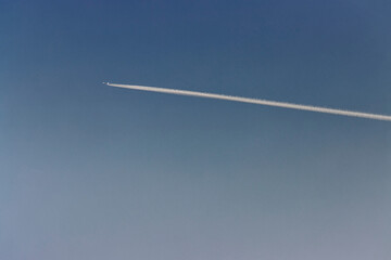 Engine exhaust contrails forming behind the airplane in a blue sky.