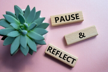 Pause and Reflect symbol. Concept words Pause and Reflect on wooden blocks. Beautiful pink...