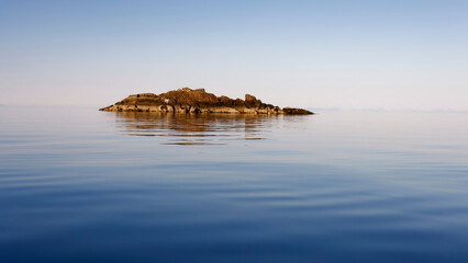 Calm sea and an islet in a warm summer day. Lofoten, Northern Norway.  - obrazy, fototapety, plakaty