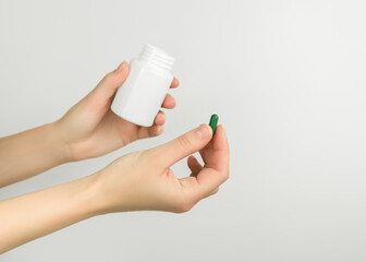 female hands holding a green pill and a white pill bottle