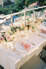 Set festive table for two with knotted napkins on plates near bouquets