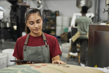 Waist up portrait of young woman looking at coffee bags during quality inspection at food...