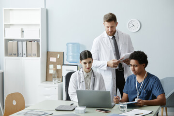 Obraz premium Multiethnic group of doctors using laptop and working together at desk in clinic, copy space