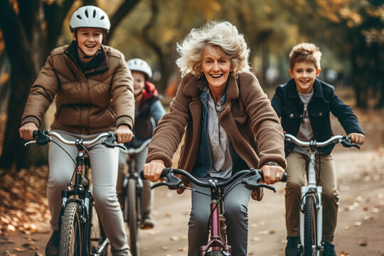 A group of family members riding bikes down a road in a park. Old woman on bike on foreground.