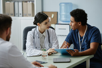Side view portrait of two young doctors discussing work issues in meeting at clinic office