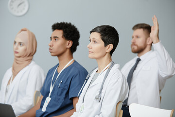 Side view portrait of diverse group of doctors sitting on chairs in audience and listening to...