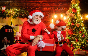 Obraz na płótnie Canvas Happy holidays. Santa Claus with little helper at home near Christmas tree. Santa man and little child boy at home. Christmas decorations. New Year surprise present. Winter sales. Christmas shopping.