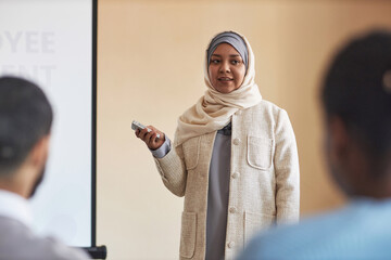 Young Muslim woman in hijab using laser pointer or switching slides on whiteboard while making...