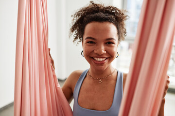 Close up portrait of young Black woman smiling in pink hammock and enjoying aerial yoga in studio