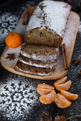 Tangerine slices, holiday cupcake, cinnamon sticks and cardamom, powdered sugar snowflakes on a dark background.